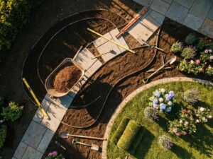Luchtfoto van tuintransformatie in uitvoering met gebogen tuinbedden, stenen paden en professionele landschapsgereedschappen